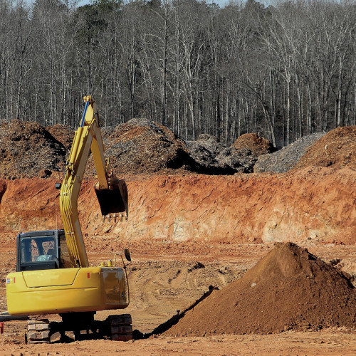 A bulldozer parked by a pile of dirt with a eastern forest in the background.